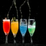 Vibrant colored cocktails splashing in glasses against a black background.