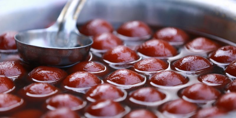 Close-up view of Gulab Jamun in a stainless steel pot, popular Indian dessert street food.